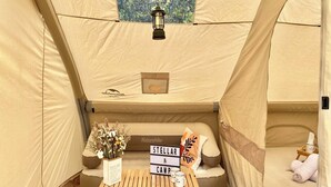 A cozy interior of a tent with a bed, a small table with a sign, and a lantern.