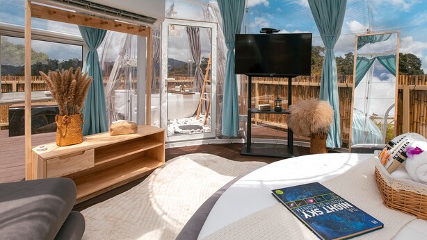 A cozy room with a large window, a flat-screen TV, a reading area with a book, and a wicker basket with towels.