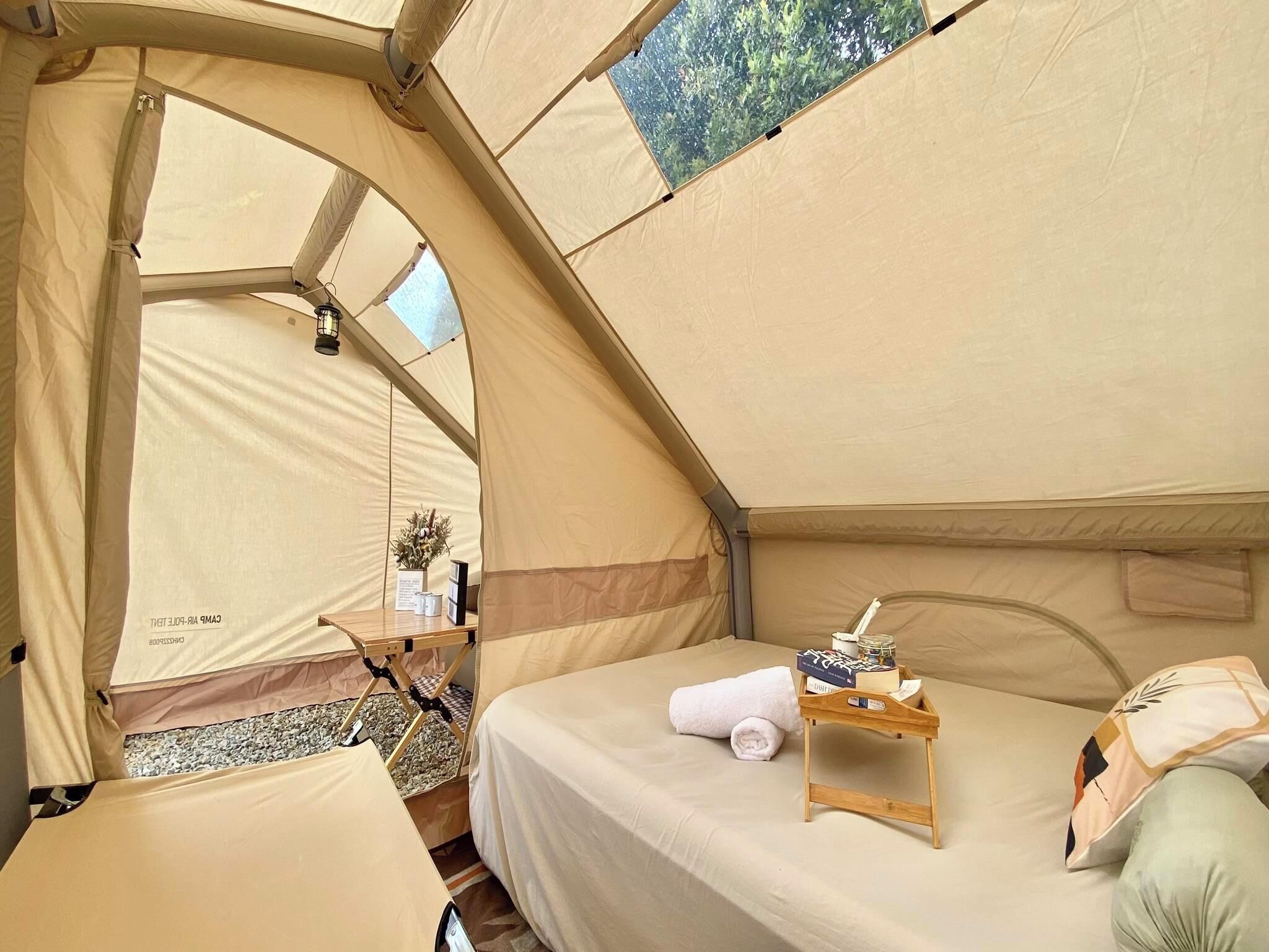 Alojamento tipo tenda com uma cama, uma pequena mesa de madeira e uma janela com vista para o verde.