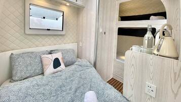 A cozy bedroom with a bed, a window, a mirror, and a built-in shelf with a kettle and other items.