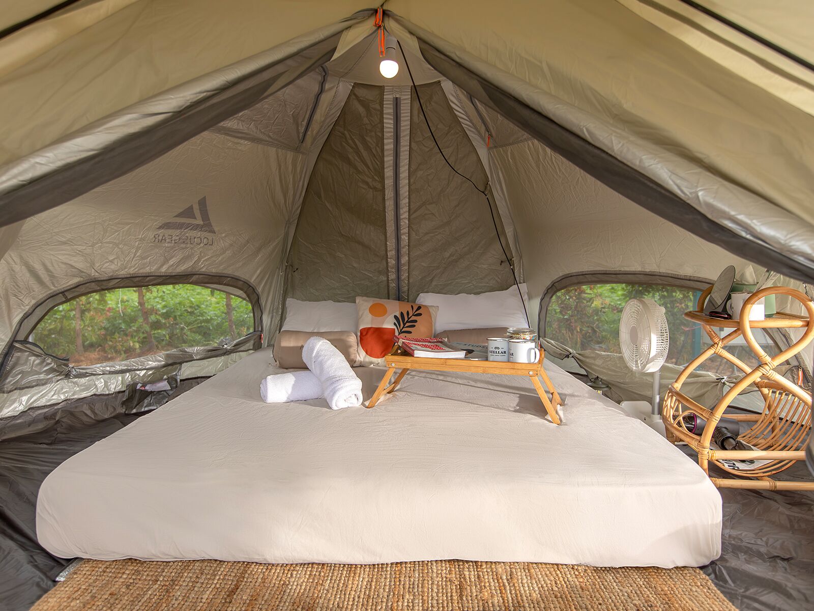 A tent with a bed, a small table, and a fan.