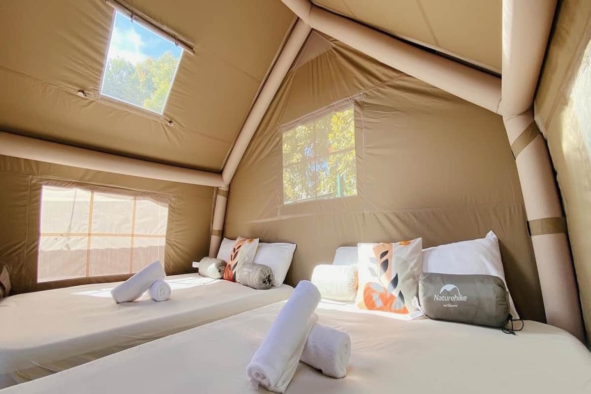 A tented accommodation with two beds, each with pillows and a rolled towel.