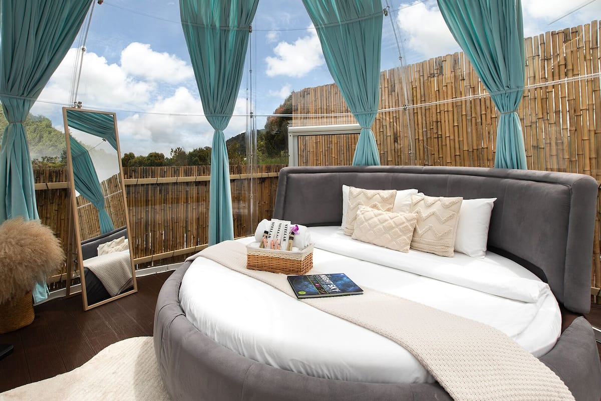 A bedroom with a large bed, a bedside table with a book, and a mirror.
