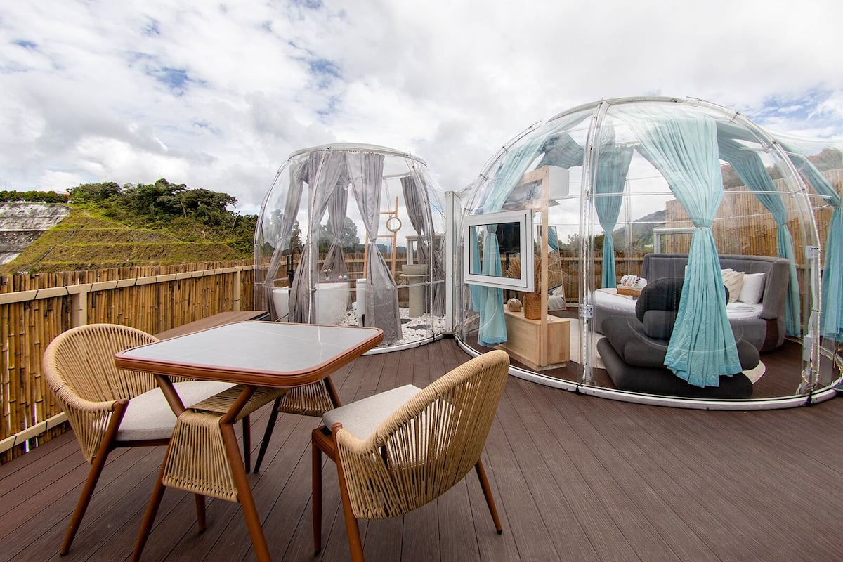 A transparent dome structure with a cushioned seating area and a table on a wooden deck.