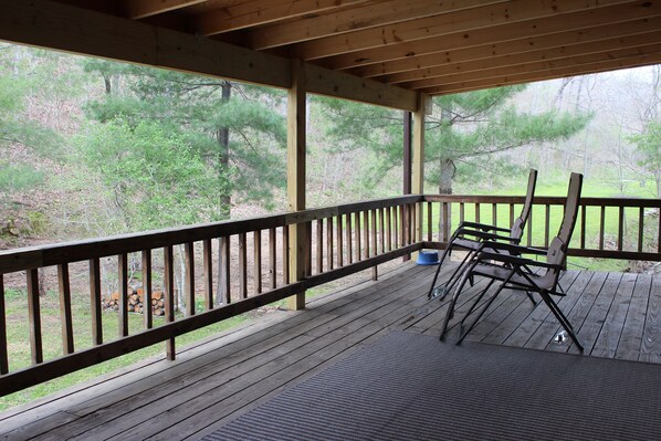 A covered deck with a wooden railing, a blue dog bowl, and two folding chairs.