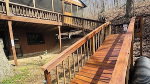 Eine Holzterrasse führt zu einer Hütte mit einer Veranda und Blick auf den umliegenden Wald.