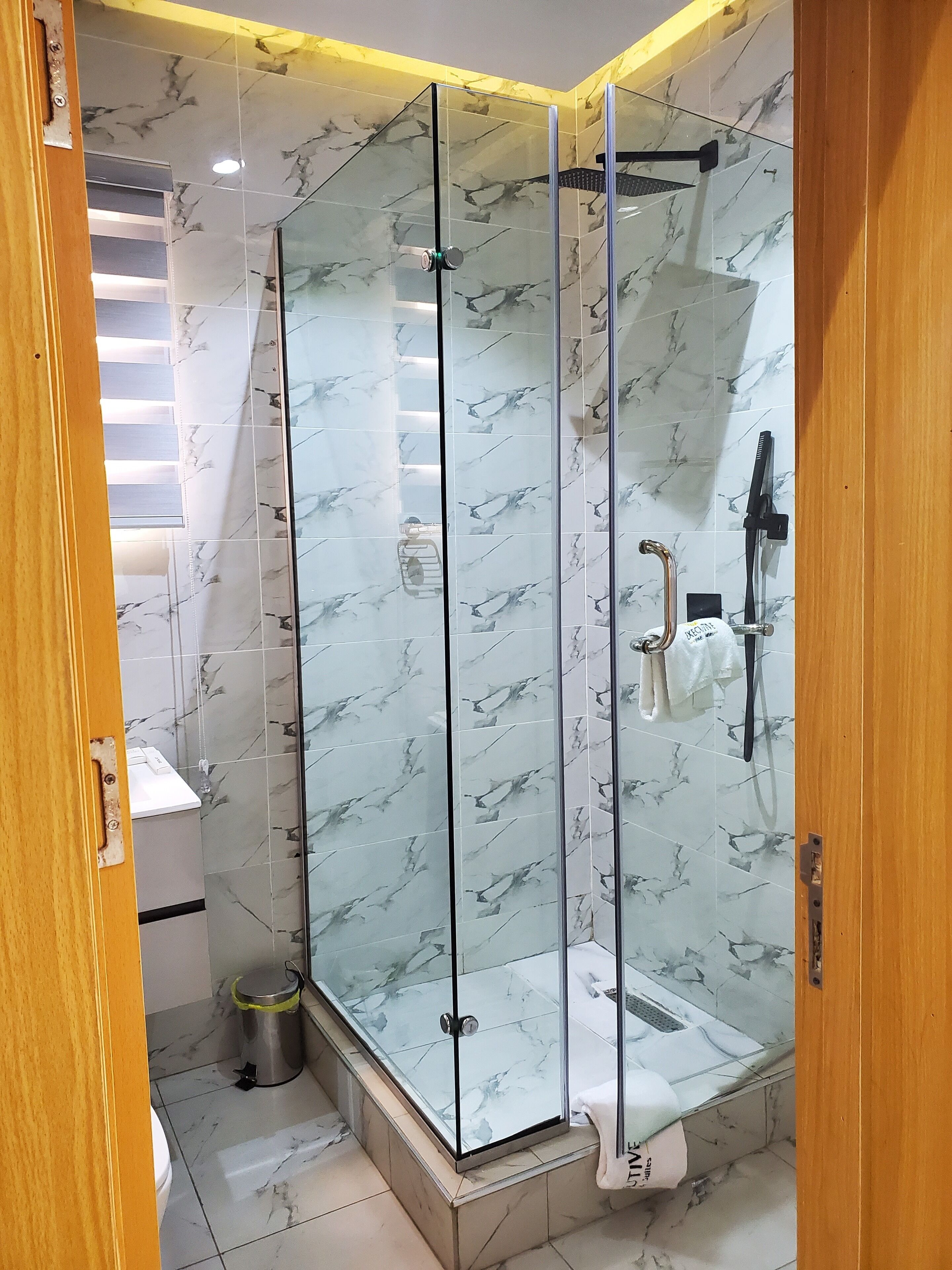 Un baño moderno con ducha de vidrio, azulejos de mármol y puerta de madera.