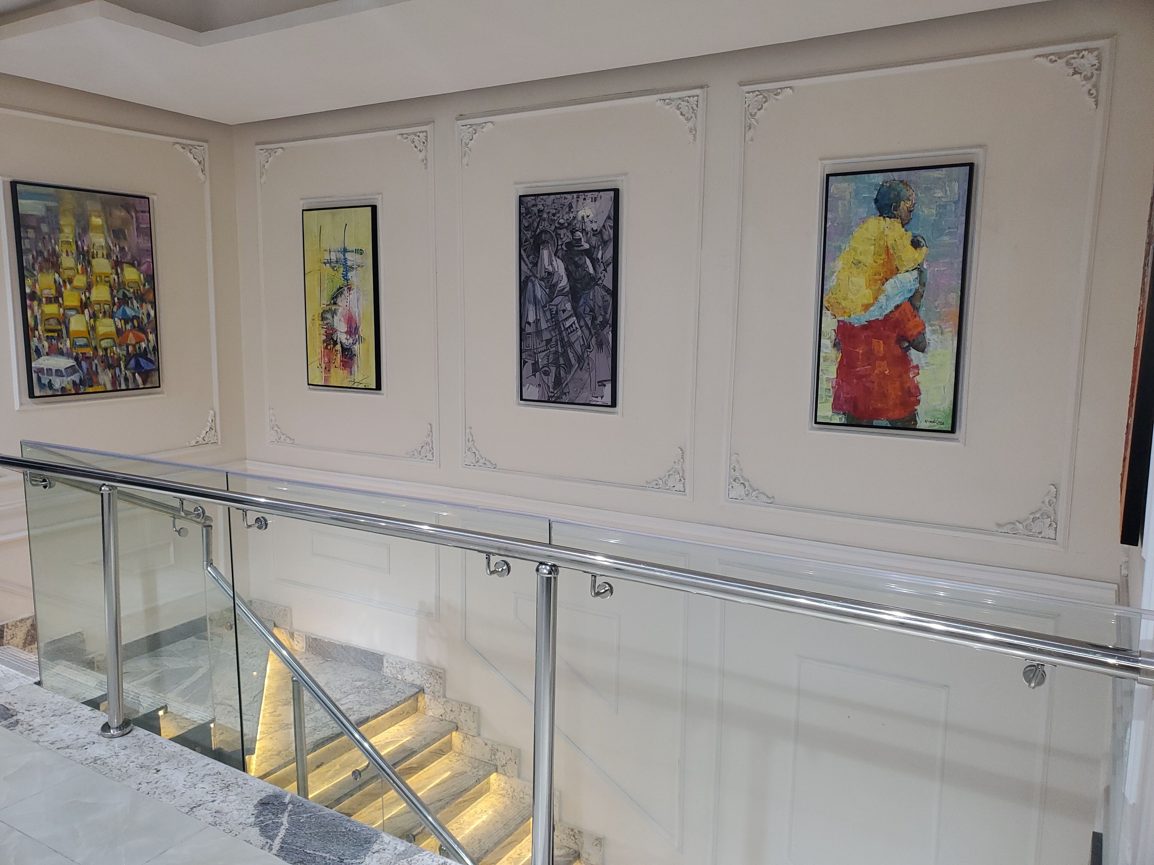 A staircase with glass railings and a series of framed artworks on the walls.