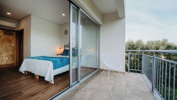 Relax on the balcony with a view of lush greenery, featuring a comfortable bed and a chair.