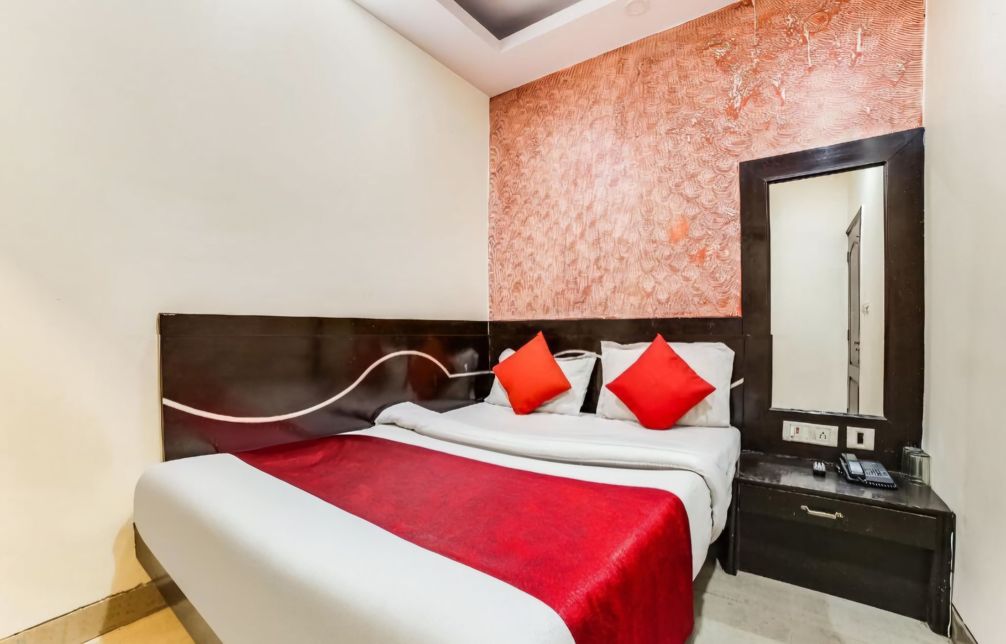 A hotel room with a bed, a nightstand, a mirror, and a patterned wall.