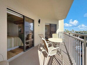 A balcony with a table and chairs, a sliding glass door leading to a room, and a view of the cityscape.