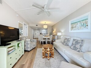 A spacious living room with a flat-screen TV, a dining area with a chandelier, and a large painting on the wall.