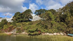 Udsigt over en sø med et hus omgivet af frodig vegetation og et flagstang med det amerikanske flag.