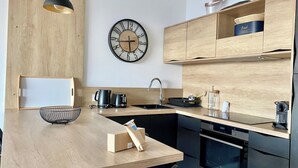 A modern kitchen with a wooden countertop, a black kettle, a coffee maker, a sink, and a clock on the wall. - 55-"Le rêve éveillé", vue mer, garage 38 (Menton)