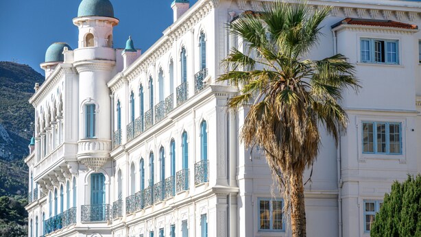 A large, ornate building with multiple balconies and a prominent palm tree in front. - 72-"Charmant studio" Plein centre, Calme, Terrasse (Menton)