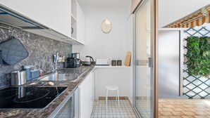 A modern kitchen with a black stove, white cabinets, and a small white stool. - 72-"Charmant studio" Plein centre, Calme, Terrasse (Menton)