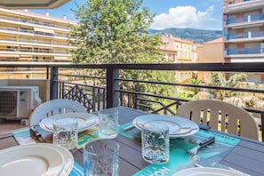 Una tavola imbandita per la cena, con piatti, bicchieri e posate, con vista su un panorama urbano che include edifici e alberi.