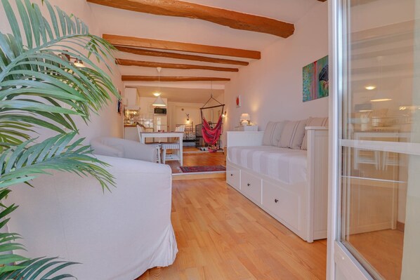 A room with a bed, a sofa, a hanging chair, a dining area, and a kitchen in the background.