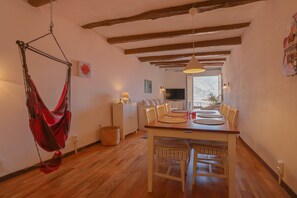 A dining area with a wooden table, chairs, a hanging red hammock, and a view to the outside.