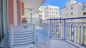 Un balcon avec une table et des chaises, une balustrade et une vue sur les bâtiments voisins.