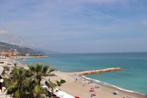 A beach with palm trees, a rocky breakwater, and a clear blue sky. - 70-2 pièces plein Centre, Terrasse, Parking (Menton)