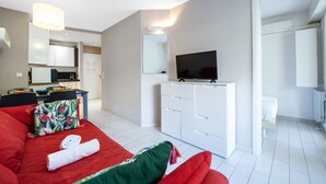 A modern hotel room with a red sofa, a white TV stand, and a dining area with a table and chairs. - 6-"Aux Rivages du Parc" Plein Centre, Calme, Plage (Menton)