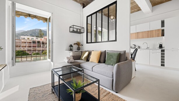 A modern living room with a sofa, a glass coffee table, and a view of the city through large windows. - 82 -L’Écrin d’Alexandra, cosy 2 pièces (Menton)