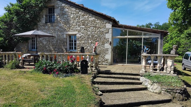Una casa de piedra con balcón, puerta de cristal y un pequeño jardín.