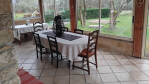Un patio cubierto con mesa y sillas, ventanas amplias y vistas a un jardín.
