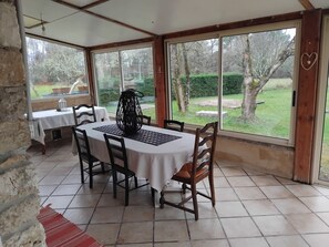 A covered patio with a table and chairs, large windows, and a view of a garden.