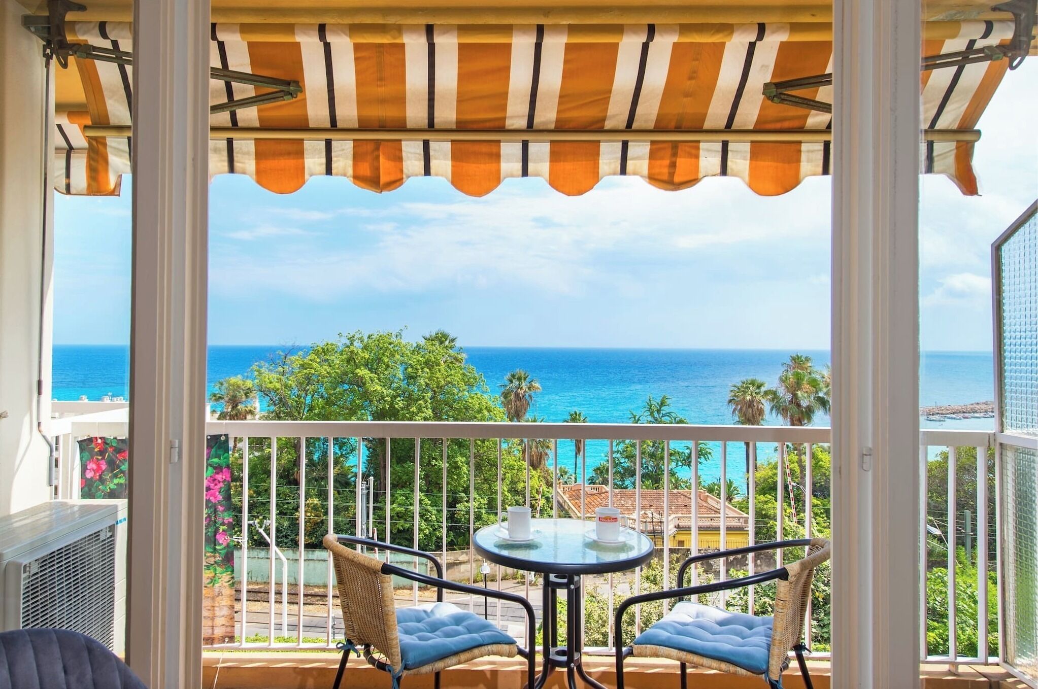 Een balkon met uitzicht op de oceaan, een tafel met stoelen en een gestreept zonnescherm.