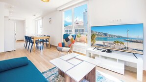 Un salon moderne doté d’un grand téléviseur, d’un coin repas et offrant une vue sur un paysage côtier.