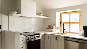 Una cocina con armarios blancos, estufa, lavavajillas y ventana con vistas al exterior.