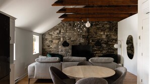 Una sala de estar moderna con una pared de piedra, techo de madera y una mesa redonda con sillas.