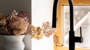Un lavamanos de cocina con un grifo moderno, una planta en maceta con flores secas y una ventana con vistas a un paisaje nevado.