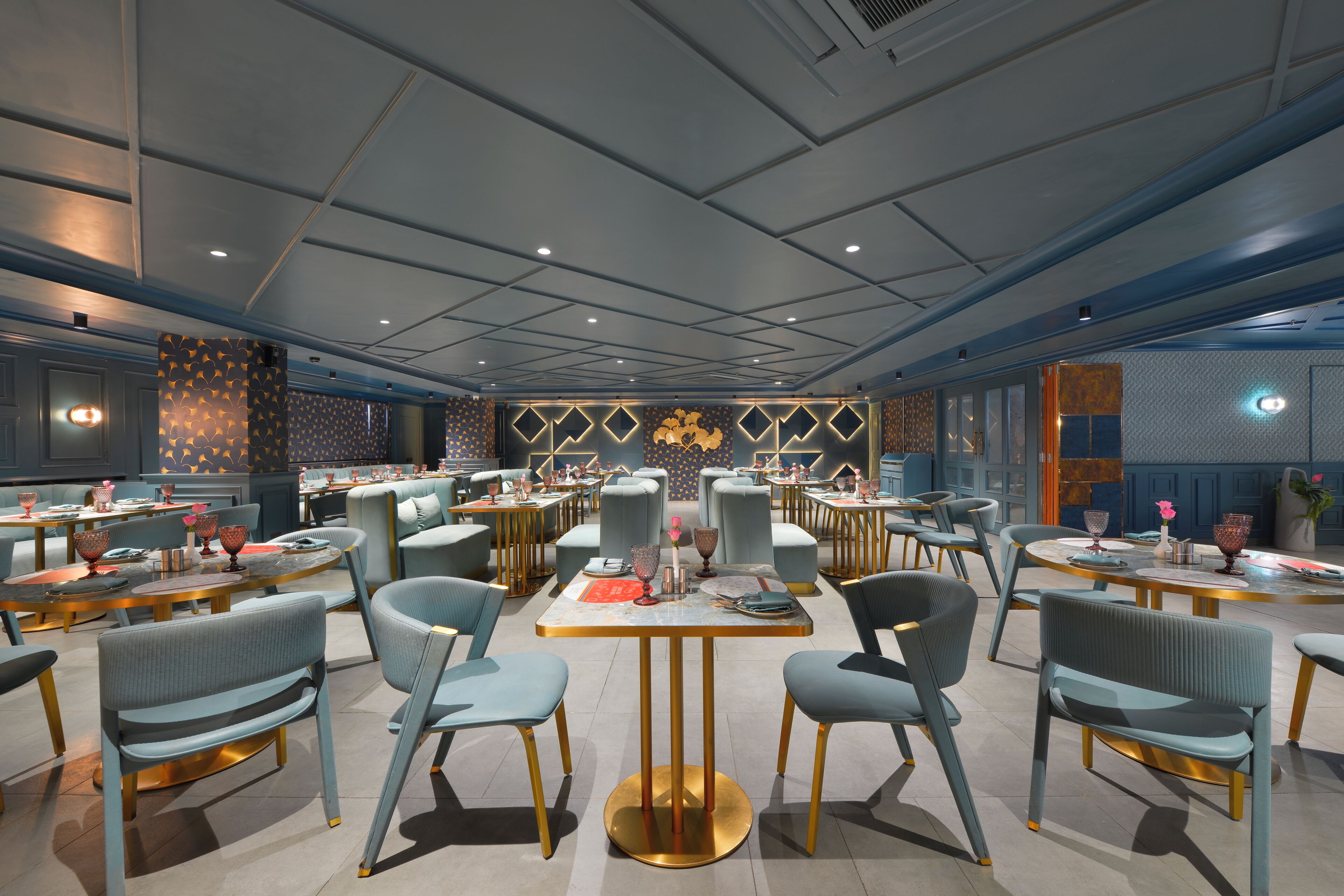 A modern restaurant with multiple dining tables and chairs, a patterned wall, and a ceiling with recessed lighting.