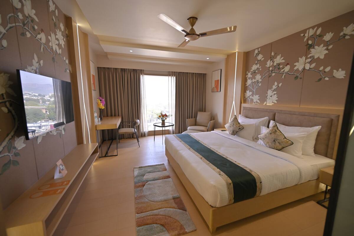 Une chambre d’hôtel avec un grand lit, un bureau, une chaise, une télévision et un ventilateur de plafond.