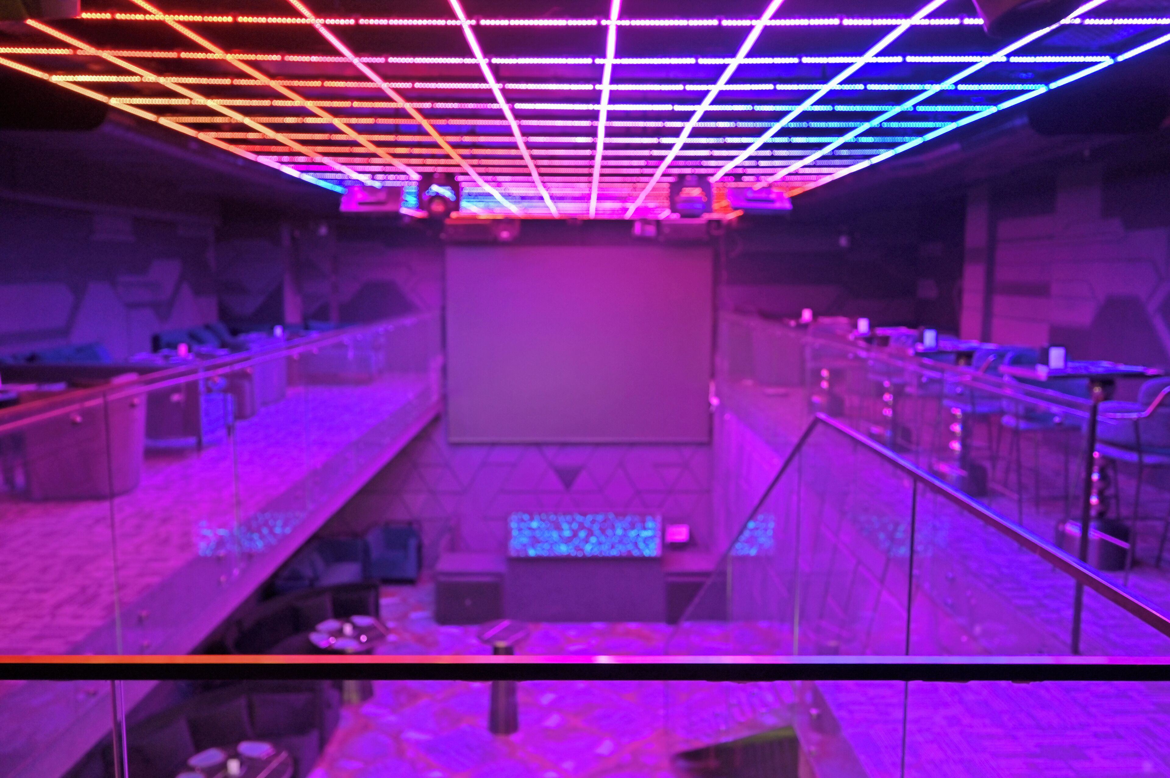 A multi-level indoor space with a grid of neon lights on the ceiling, seating areas, and a stage at the front.