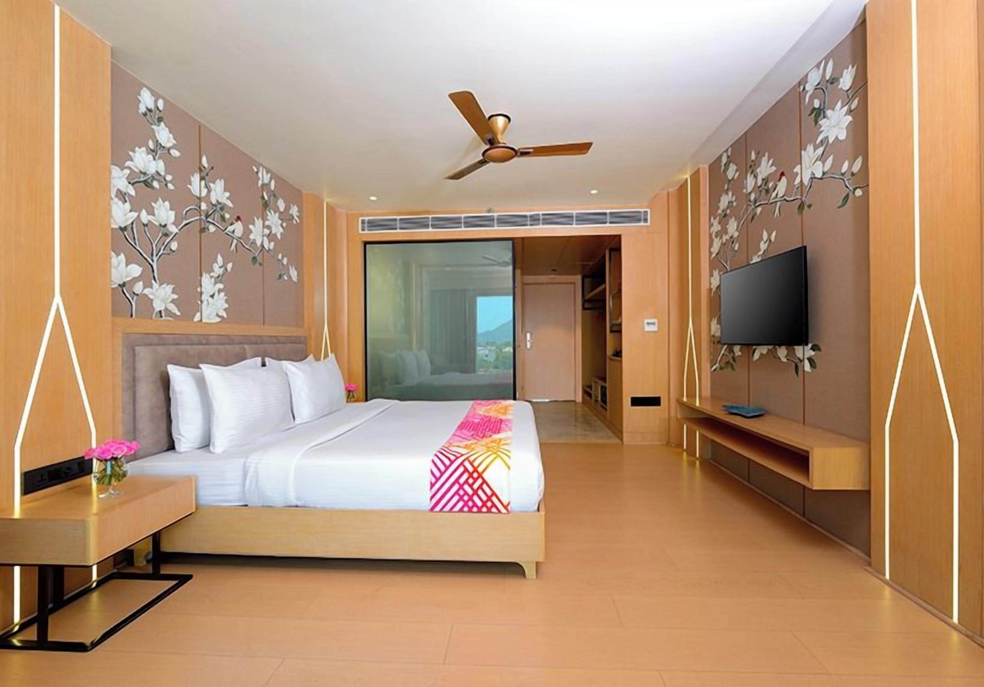 Una habitación de hotel con una cama, televisión, escritorio y un ventanal grande.