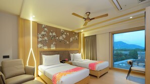 A hotel room with two beds, a sofa, a ceiling fan, and a large window with a view. - Ginger Ajmer Hathi Bhata (Ajmer)
