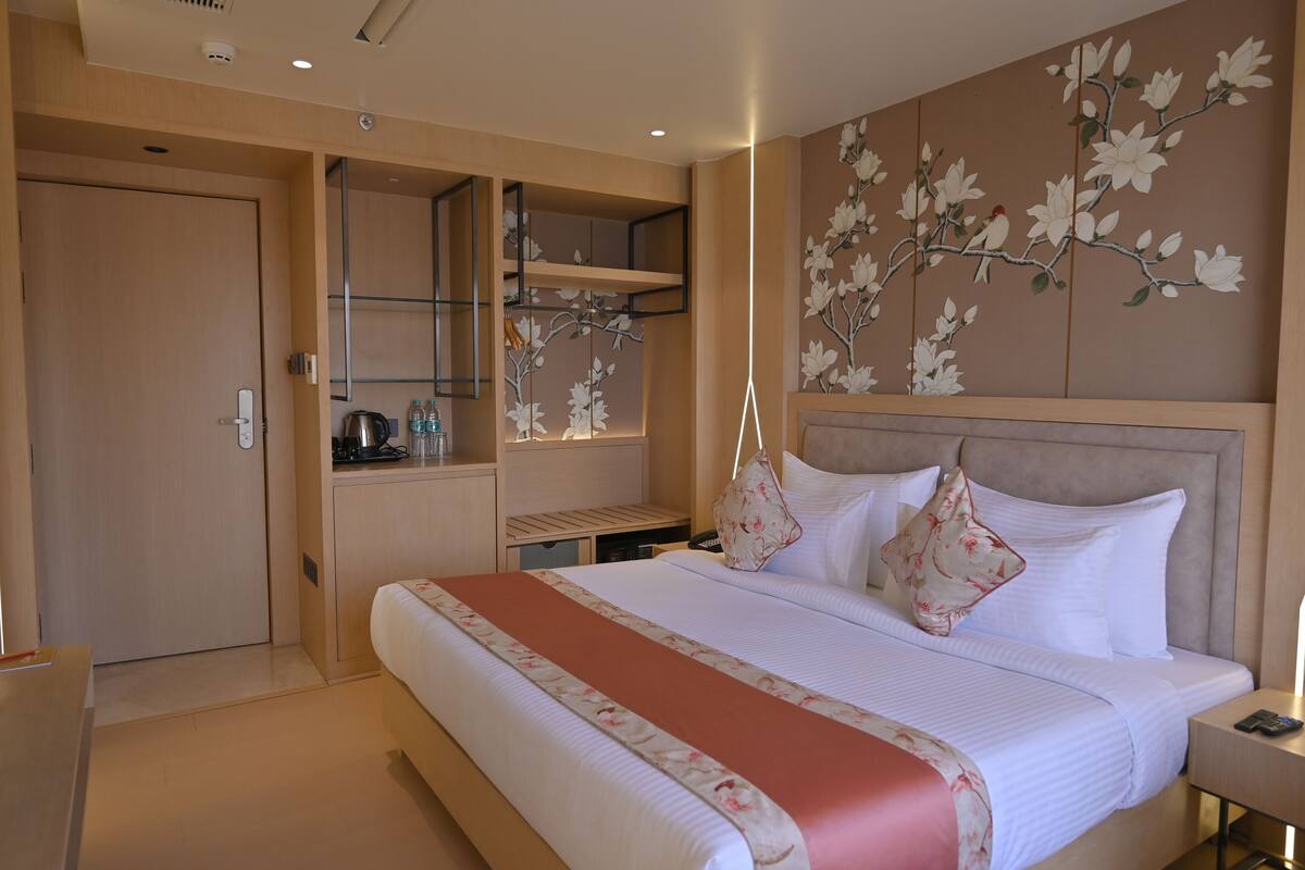 Une chambre d’hôtel avec un grand lit, une armoire, un petit bureau et un mur orné d’une fresque florale.