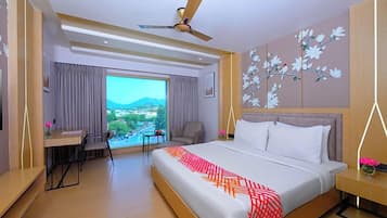 A hotel room with a bed, a desk, a chair, a view of the outdoors, and a ceiling fan.