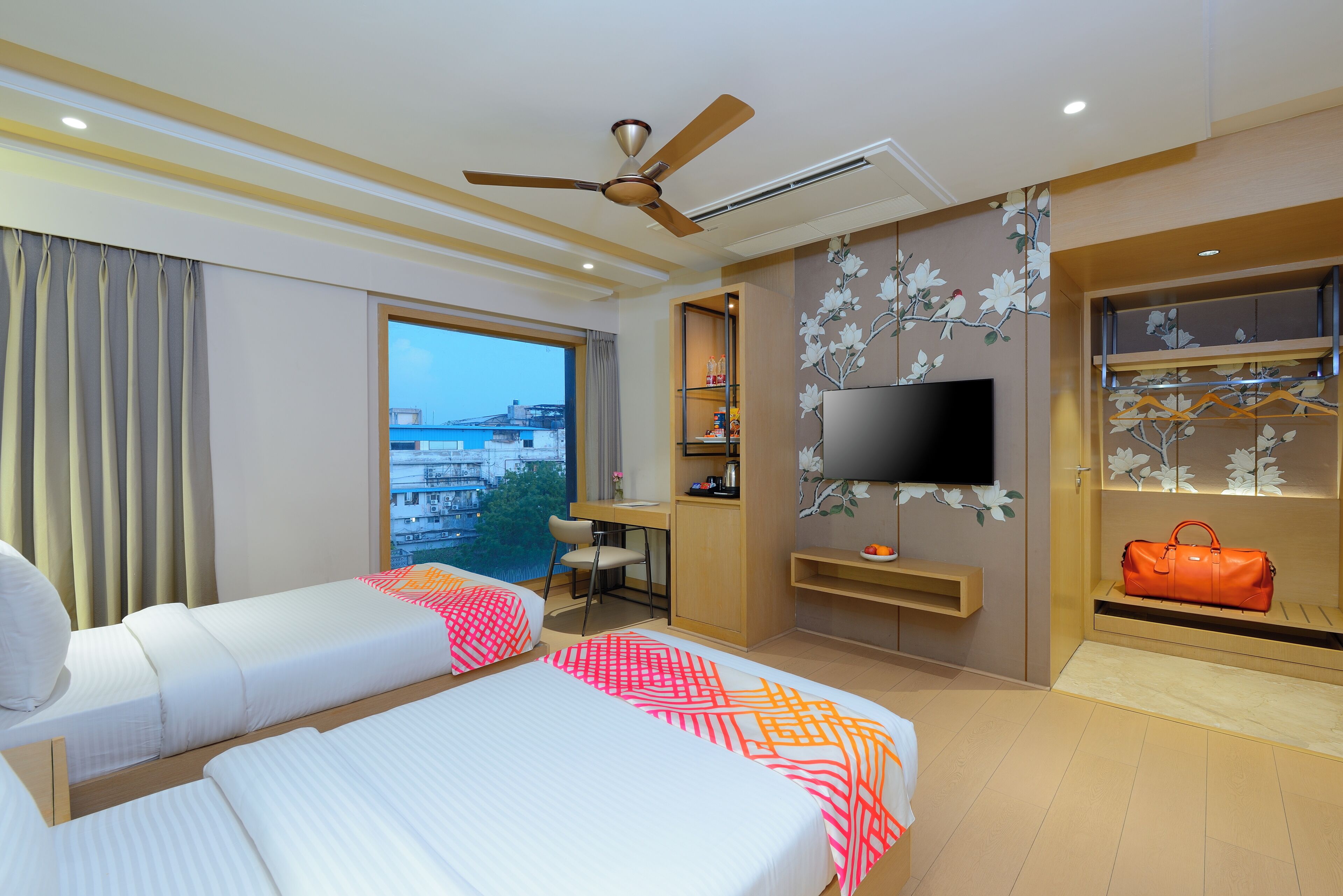 Habitación de hotel con dos camas, un escritorio, un televisor y vistas a la ciudad.