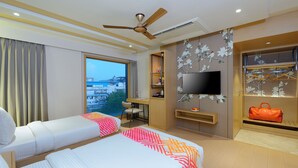 A hotel room with two beds, a desk, a television, and a view of the city.
