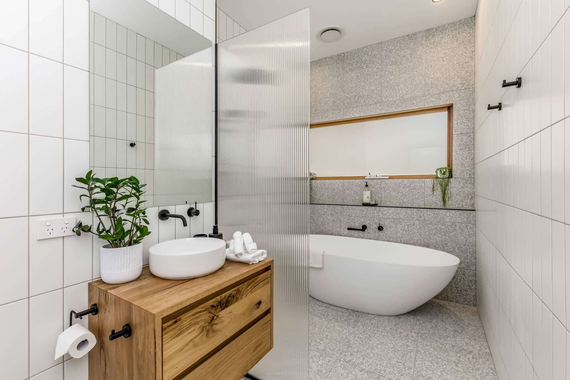 Un baño moderno con una bañera independiente, un tocador de madera con lavabo blanco y un espejo grande.