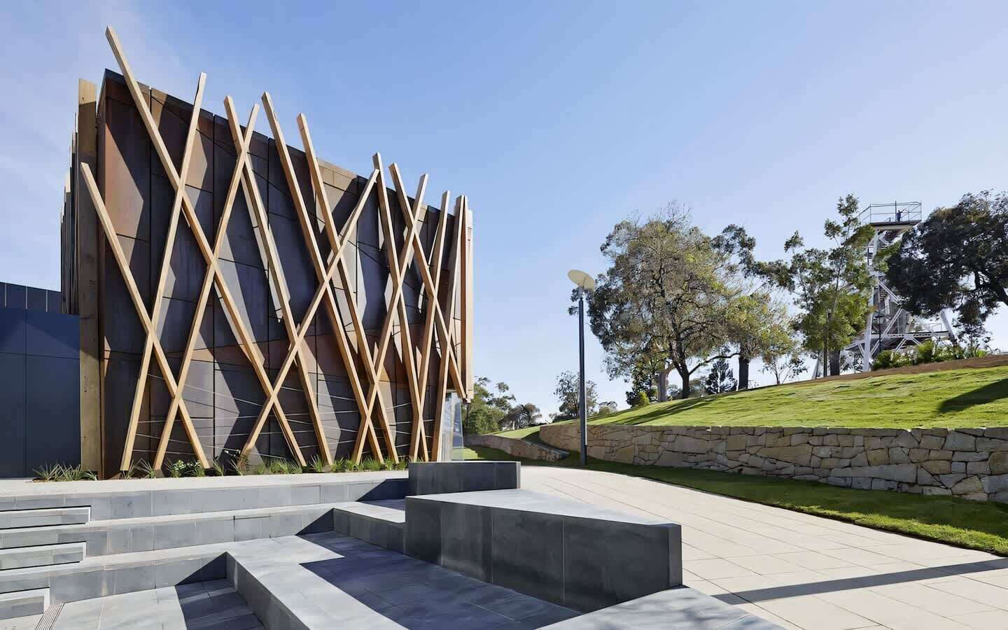 A modern building with a unique geometric facade, a stone retaining wall, and a landscaped area with steps leading to the entrance.