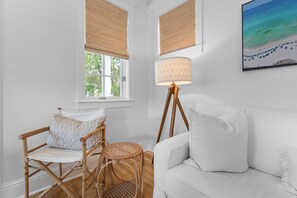 Una habitación con un sofá blanco, una silla de mimbre, una lámpara de pie y una ventana con persianas.