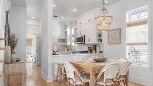 A modern kitchen with white cabinetry, a wooden dining table, and wicker chairs. - GemStone Cottage! Special Deals! Private Beach, Lux Home w/Free Bch Service! (Panama City Beach)