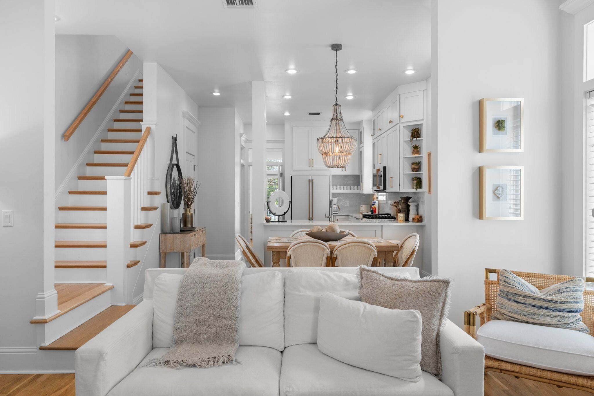 A modern interior with a staircase, a dining area, and a living room with a sofa and a wicker chair.