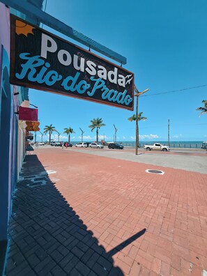 A sign for 'Pousada Rio do Prado' with a clear view of the beach and palm trees in the background. - Pousada Rio do Prado (Porto Seguro)